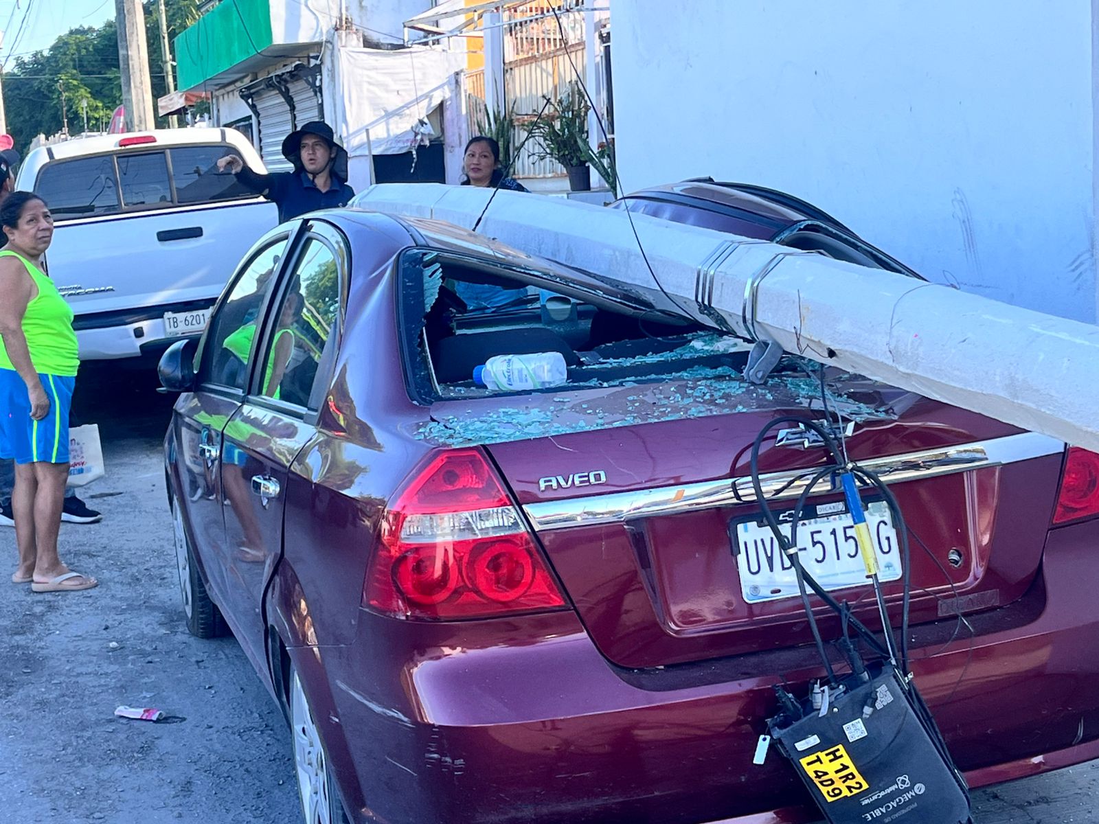 Tras atorarse en los cables, tráiler derriba poste y este cae sobre un automóvil.